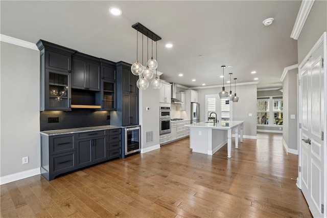 kitchen with wine cooler, ornamental molding, stainless steel appliances, light wood-type flooring, and a sink