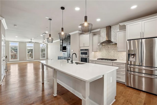 kitchen with a sink, wood finished floors, appliances with stainless steel finishes, wall chimney range hood, and backsplash