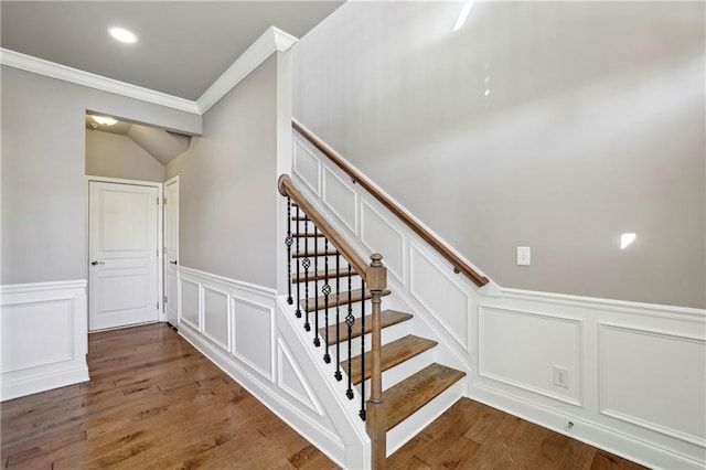 stairway with ornamental molding, a wainscoted wall, a decorative wall, and wood finished floors