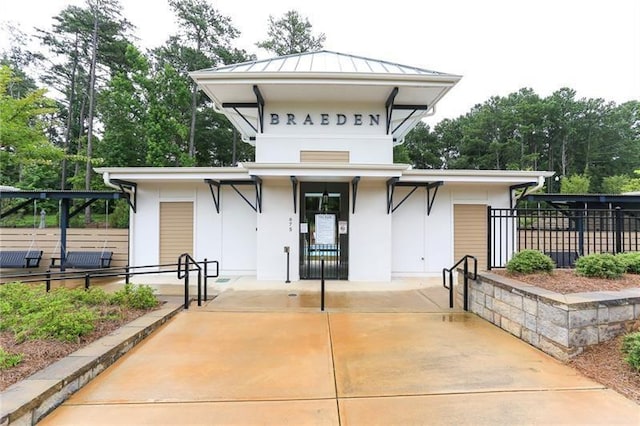 rear view of property with a standing seam roof, fence, metal roof, and stucco siding