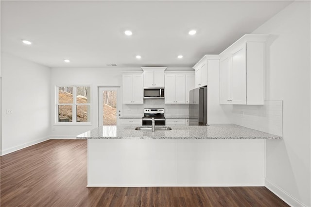 kitchen with a sink, light stone counters, backsplash, white cabinetry, and appliances with stainless steel finishes