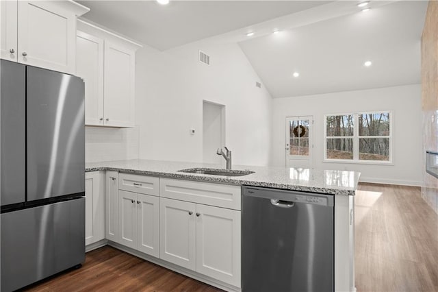 kitchen with visible vents, vaulted ceiling, a peninsula, stainless steel appliances, and a sink