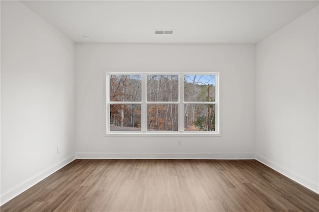 empty room featuring wood finished floors, visible vents, and baseboards