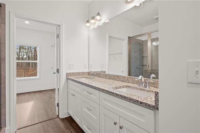 full bathroom featuring double vanity, a stall shower, wood finished floors, and a sink