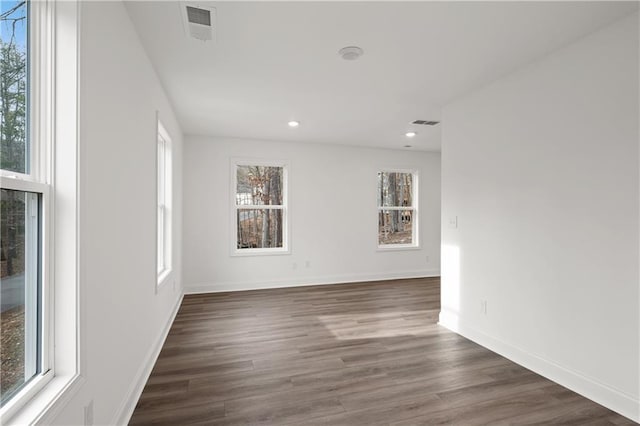 empty room with dark wood finished floors, visible vents, and baseboards