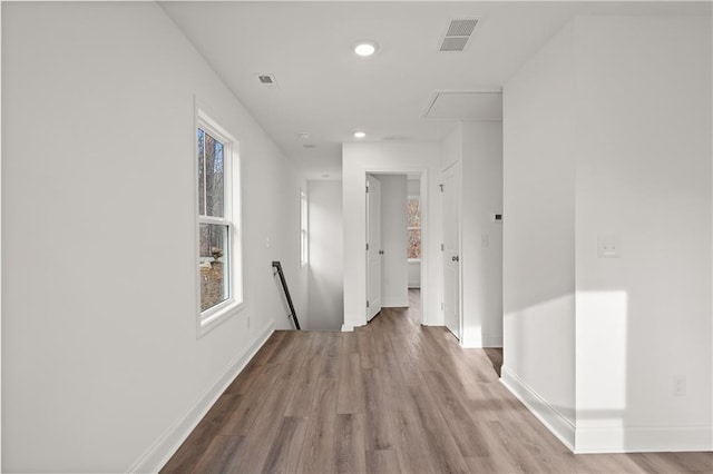 hallway featuring wood finished floors, visible vents, baseboards, attic access, and an upstairs landing