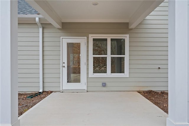 view of exterior entry featuring a patio and roof with shingles