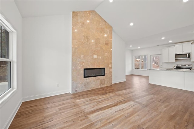 unfurnished living room with recessed lighting, baseboards, a tiled fireplace, and light wood finished floors