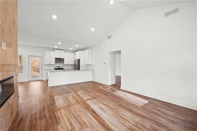 unfurnished living room featuring a tiled fireplace, visible vents, baseboards, and wood finished floors