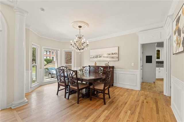 dining area featuring light wood-type flooring, ornamental molding, a chandelier, and ornate columns