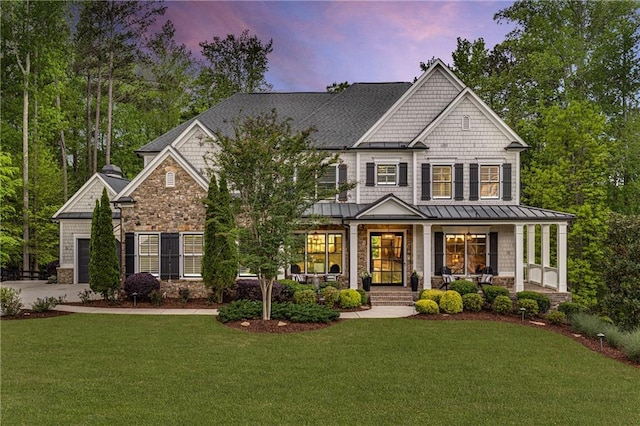 craftsman-style house featuring a front lawn, stone siding, a garage, a standing seam roof, and covered porch