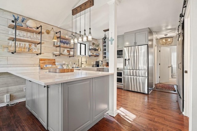 kitchen with kitchen peninsula, dark hardwood / wood-style flooring, a barn door, and appliances with stainless steel finishes