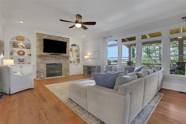 living room with plenty of natural light, a ceiling fan, a fireplace, and built in shelves