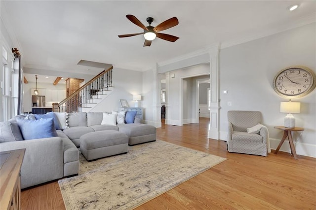 living area with ceiling fan, crown molding, stairs, and light wood-style floors