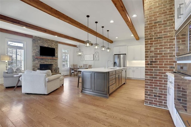 kitchen featuring stainless steel appliances, a stone fireplace, light wood-style floors, open floor plan, and white cabinetry