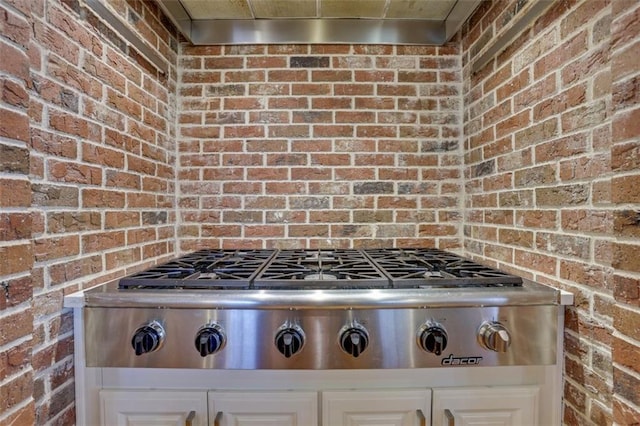 details with stainless steel gas stovetop, range hood, and white cabinetry