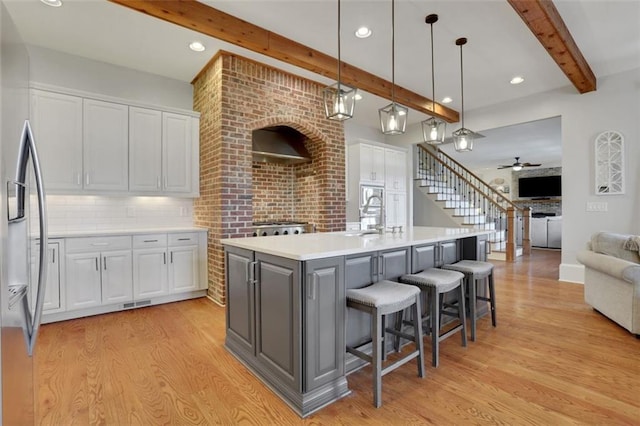 kitchen featuring beamed ceiling, light wood-type flooring, stainless steel refrigerator with ice dispenser, and white cabinets