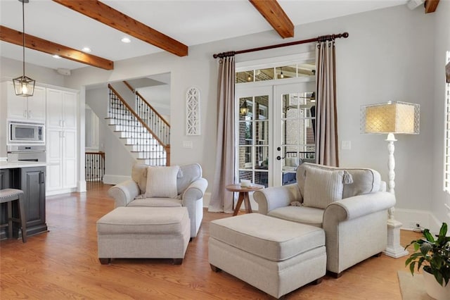 living area with baseboards, beam ceiling, and light wood-style floors