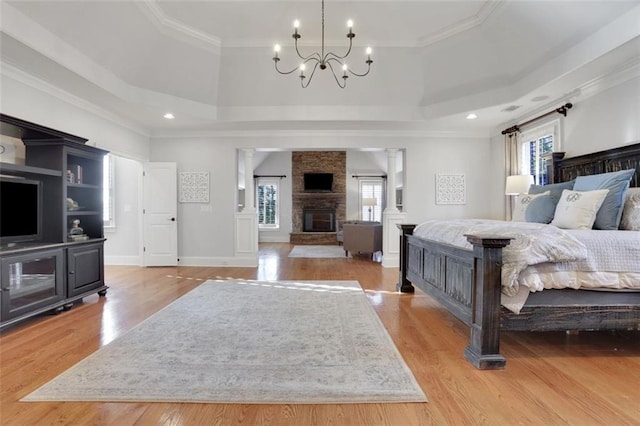 bedroom with a stone fireplace, light wood finished floors, multiple windows, and an inviting chandelier