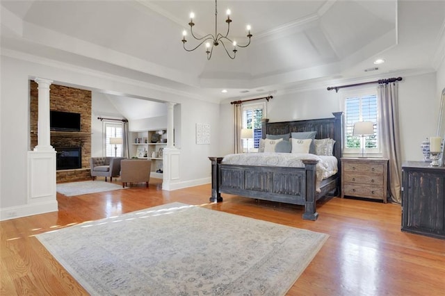 bedroom featuring a stone fireplace, ornate columns, light wood-style flooring, and an inviting chandelier