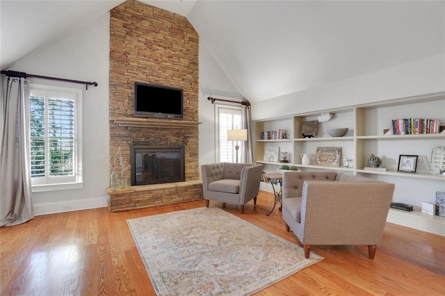 living room with light wood-type flooring, baseboards, built in features, a stone fireplace, and high vaulted ceiling