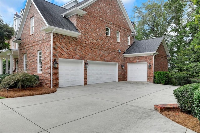 view of side of home featuring brick siding, driveway, a shingled roof, and a garage