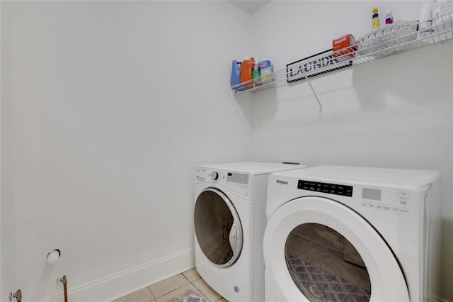 clothes washing area with light tile patterned floors, baseboards, washer and dryer, and laundry area