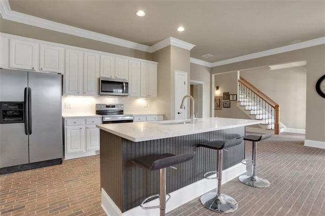 kitchen with a kitchen bar, white cabinetry, stainless steel appliances, and a sink