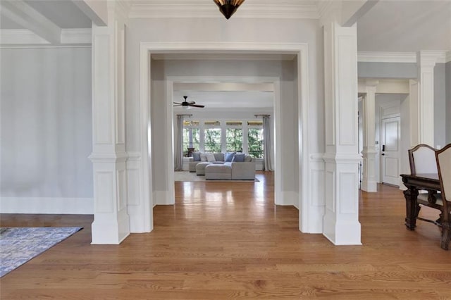 entrance foyer featuring a ceiling fan, crown molding, light wood finished floors, and ornate columns