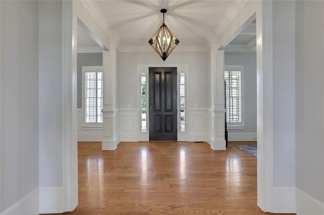 foyer entrance featuring an inviting chandelier, wood finished floors, a decorative wall, crown molding, and wainscoting