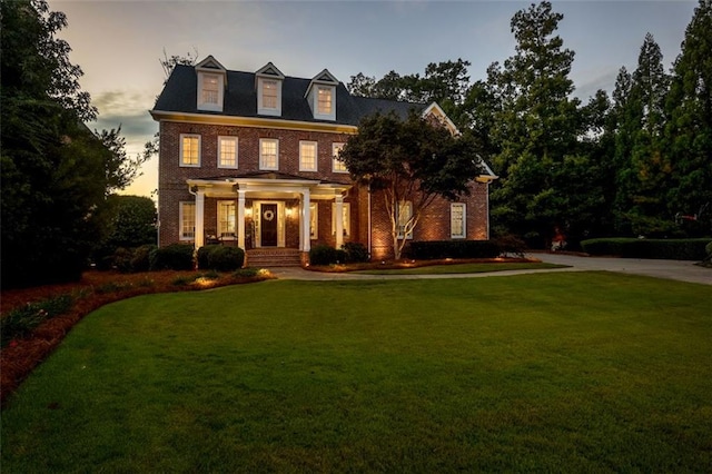 view of front of house with brick siding, a yard, and covered porch