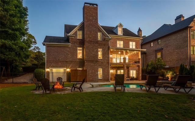back of property with fence, a balcony, a yard, a patio area, and a fire pit