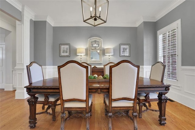 dining space featuring wood finished floors, a notable chandelier, ornamental molding, and a decorative wall