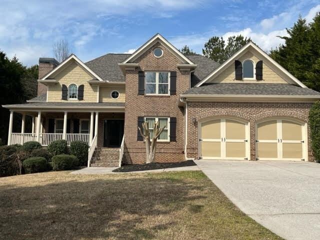 view of front facade featuring a porch, an attached garage, brick siding, driveway, and a chimney