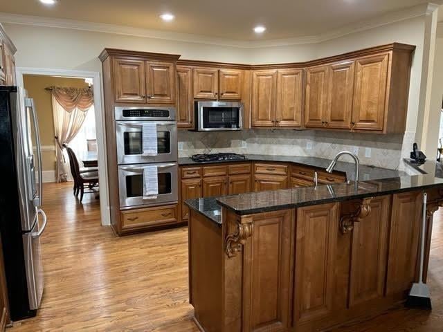 kitchen with brown cabinets, light wood finished floors, stainless steel appliances, a sink, and a peninsula