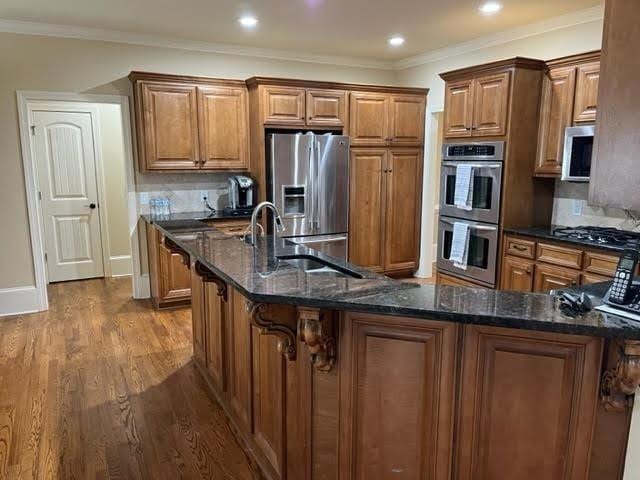 kitchen with dark wood-style floors, appliances with stainless steel finishes, brown cabinetry, and ornamental molding