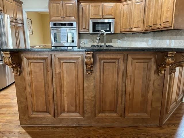 kitchen with light wood-style flooring, a sink, appliances with stainless steel finishes, backsplash, and brown cabinetry