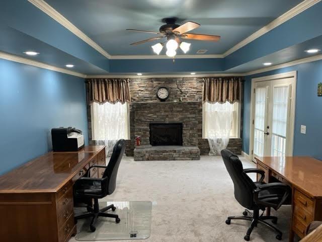 carpeted home office featuring a ceiling fan, a fireplace, a tray ceiling, and crown molding