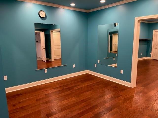 empty room with crown molding, baseboards, wood finished floors, and recessed lighting