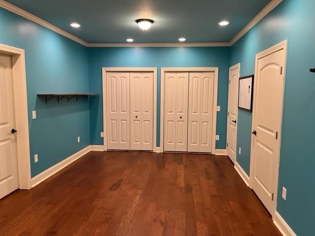 unfurnished bedroom with baseboards, two closets, dark wood finished floors, and crown molding