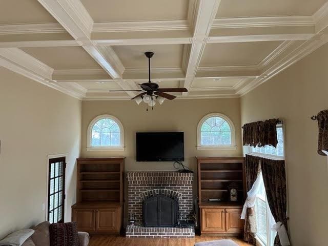 living area with a healthy amount of sunlight, a brick fireplace, coffered ceiling, and wood finished floors