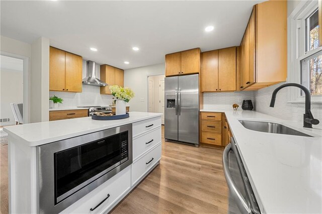 kitchen featuring wall chimney exhaust hood, sink, white cabinetry, light wood-type flooring, and stainless steel appliances