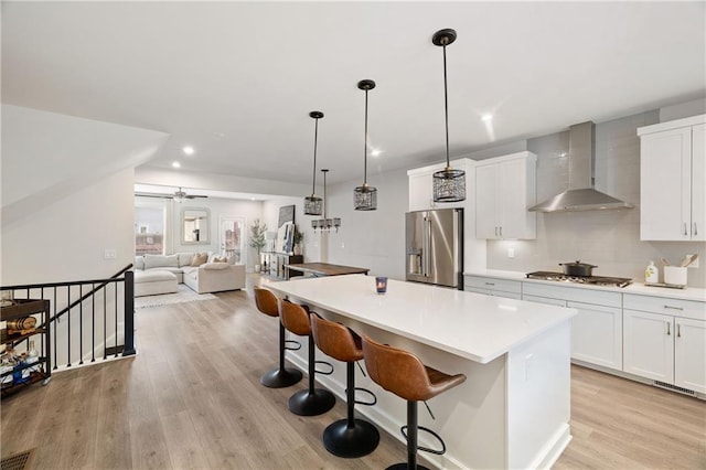 kitchen featuring a center island, appliances with stainless steel finishes, white cabinetry, light wood-type flooring, and wall chimney exhaust hood