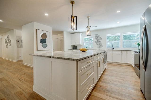 kitchen featuring white cabinets, light stone countertops, light wood-style floors, a kitchen island, and recessed lighting