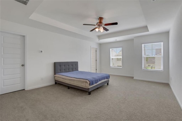 carpeted bedroom with ceiling fan and a tray ceiling