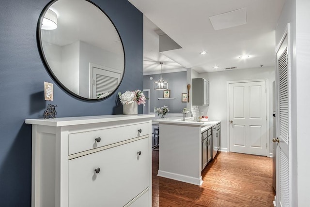 kitchen with visible vents, light countertops, a sink, wood finished floors, and a peninsula