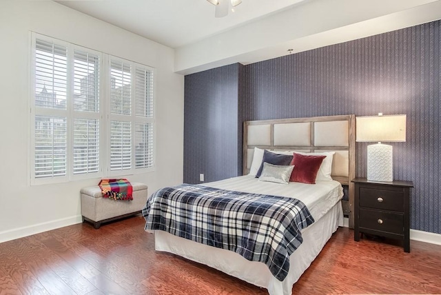 bedroom featuring an accent wall, wallpapered walls, baseboards, and wood finished floors