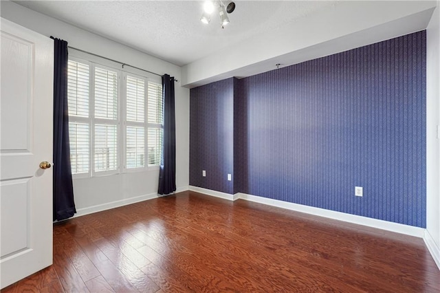 unfurnished room with baseboards, dark wood-type flooring, a textured ceiling, and wallpapered walls