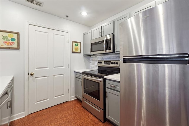 kitchen with stainless steel appliances, wood finished floors, light countertops, gray cabinets, and tasteful backsplash