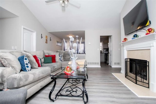 living room with a fireplace, lofted ceiling, visible vents, a ceiling fan, and wood finished floors